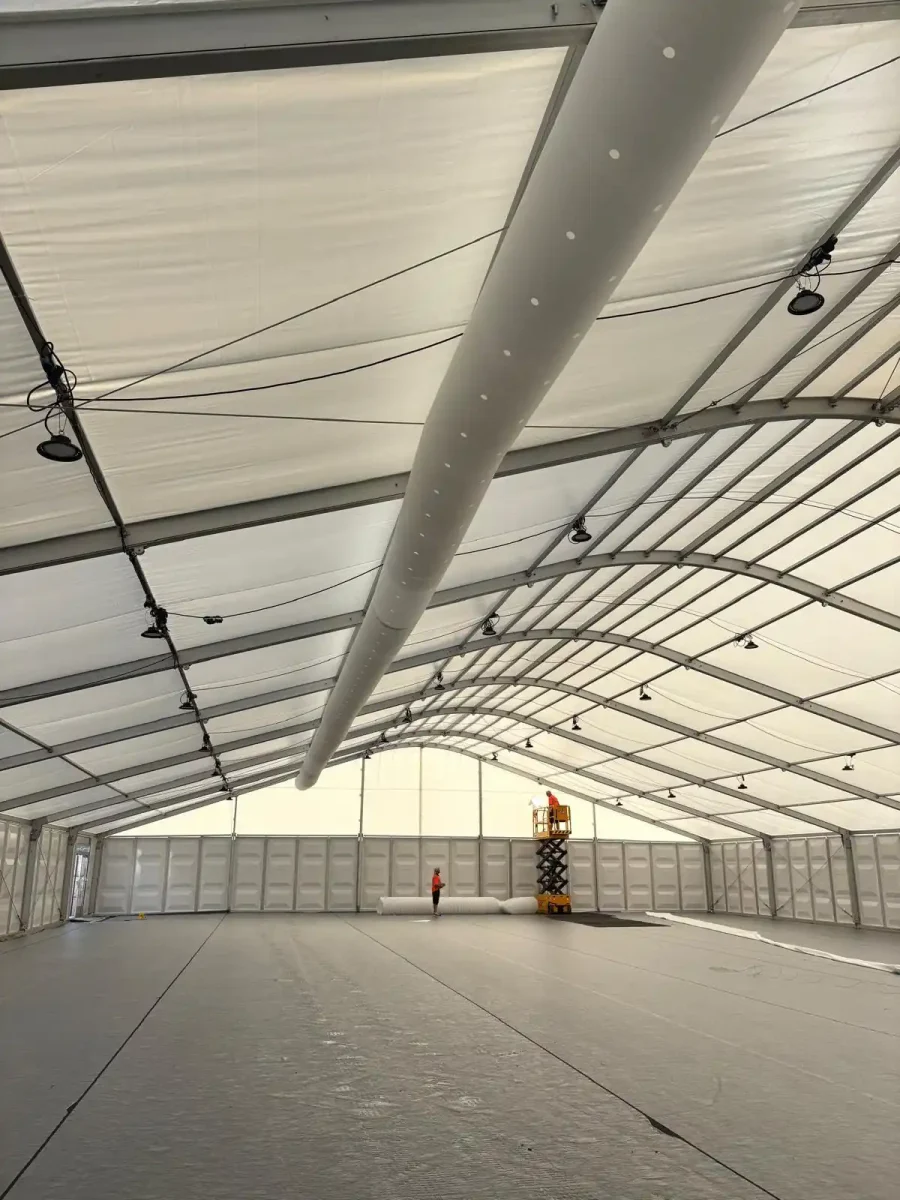 Completed overhead cooling installation inside large event marquee Interior view of a large white event marquee with overhead air conditioning ducting installed along the roof structure, floor completely clear