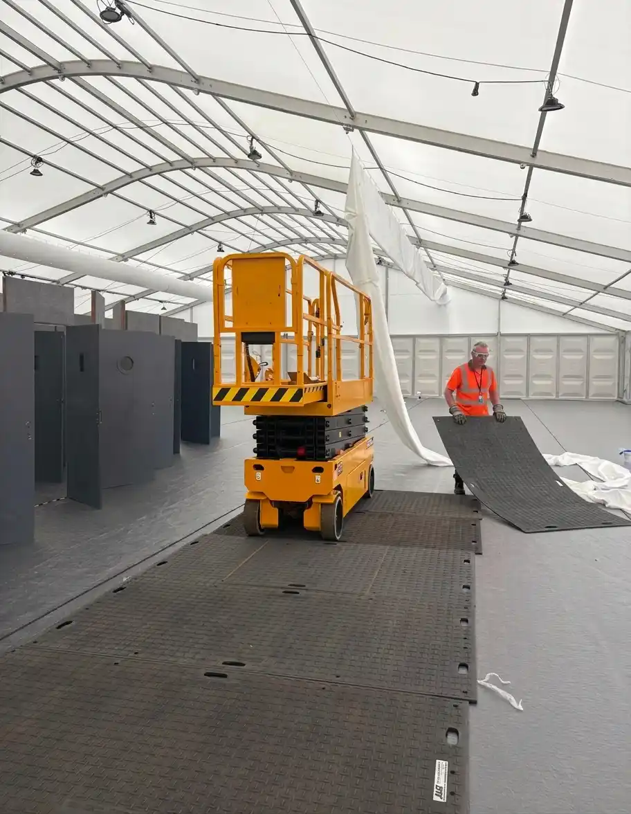 Engineer using scissor lift to install overhead ducting in event marquee Andrews Air Conditioning engineer on a scissor lift installing overhead cooling ducting inside a backstage event marquee