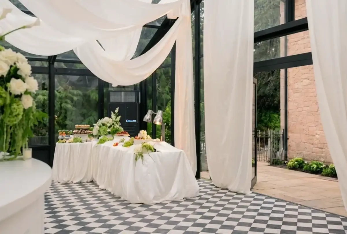 Black and white styled wedding reception inside a glass marquee, with the air handling unit blending into the venue's black window frames