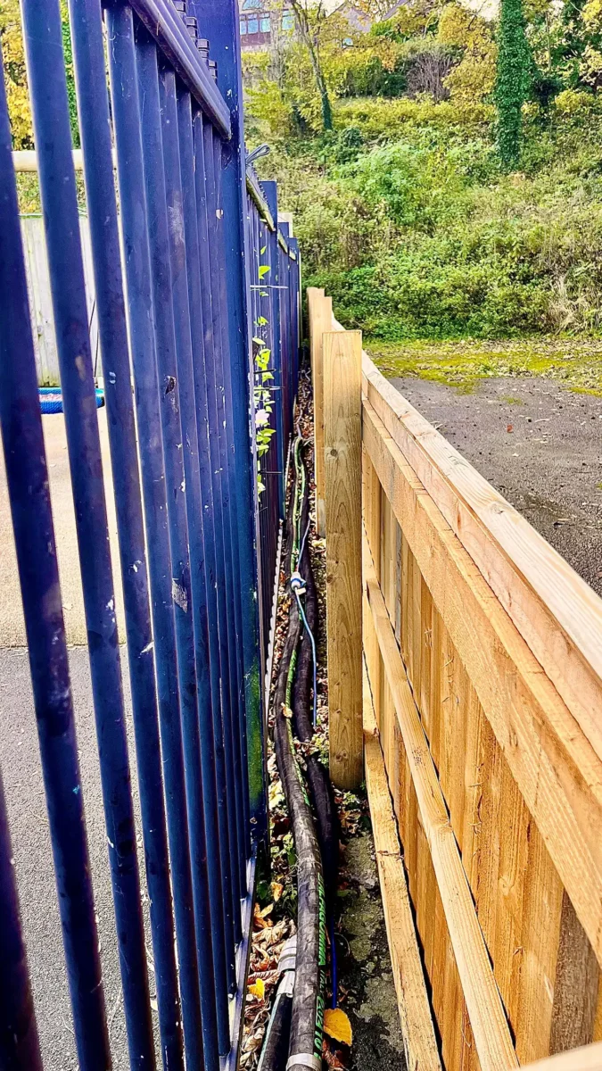 Heating pipework routed through a narrow gap between school railings and new fencing