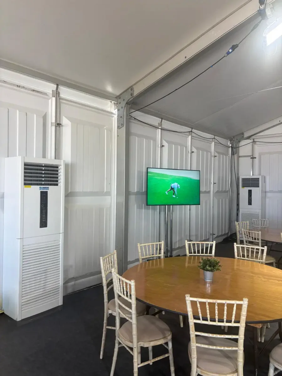 temporary event cooling for golf marquee Two air conditioning units providing temporary event cooling inside a golf event marquee with seating and television screen.